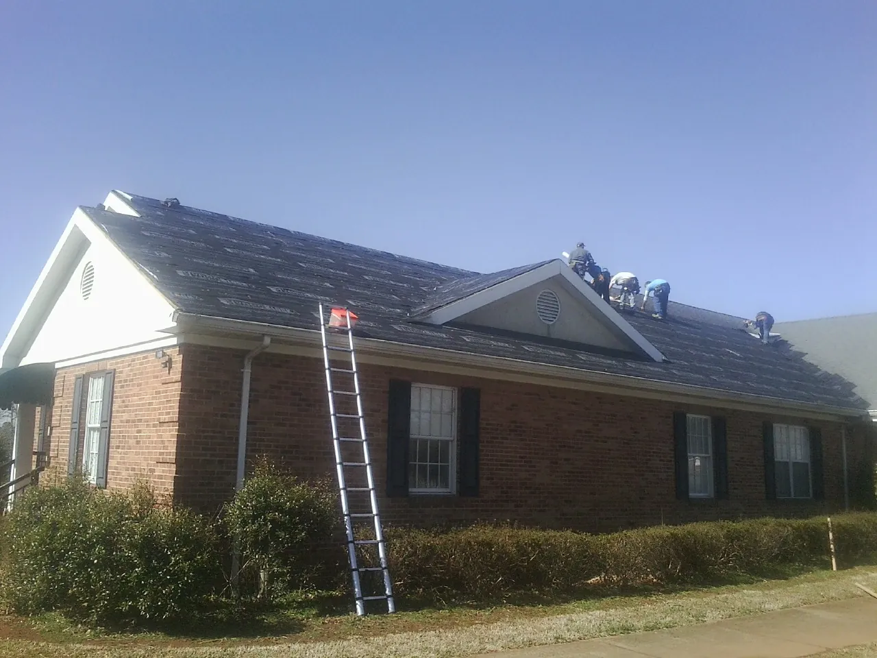 Crew tearing shingles off a brick ranch roof with a ladder set — Emergency Roof Repair work by our crew in San Jacinto