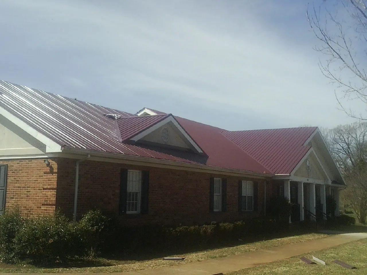 Red metal roof with gabled entries on a long brick building, from a Hail Damage Roof Repair job in San Jacinto