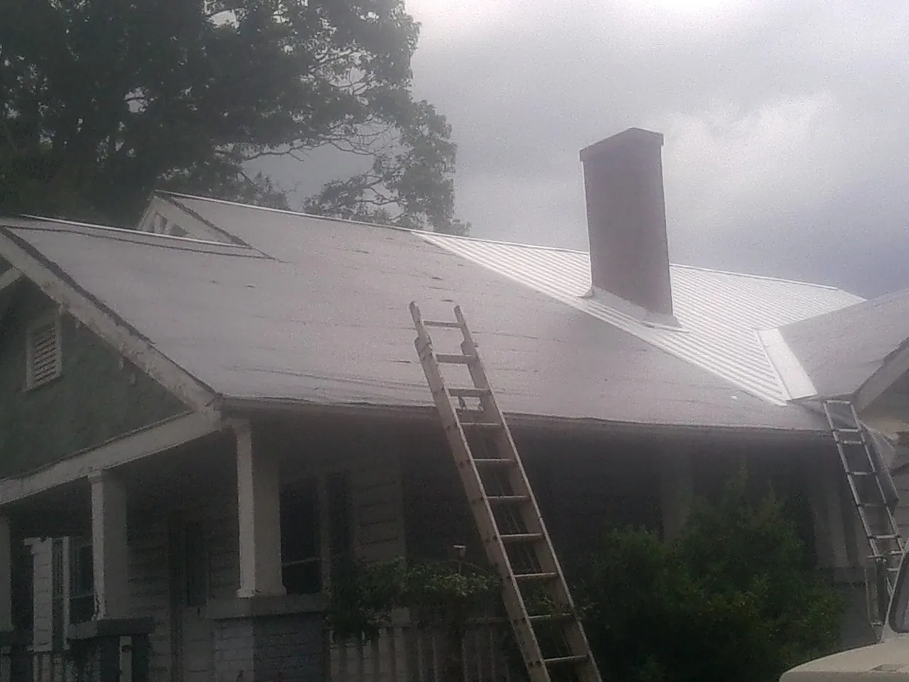 Ladders against a metal roof on an older home with a brick chimney in San Jacinto