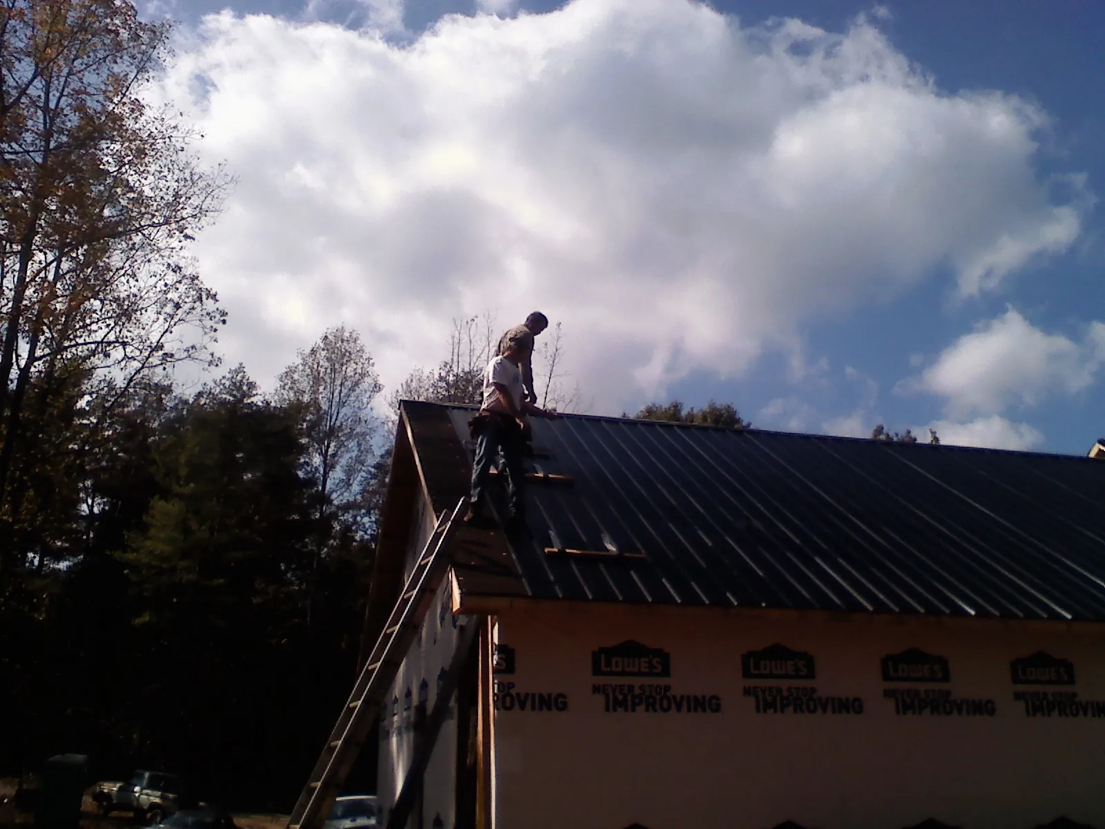Roofer fastening dark metal panels high against a cloudy sky, from a Roof Inspection job in San Jacinto