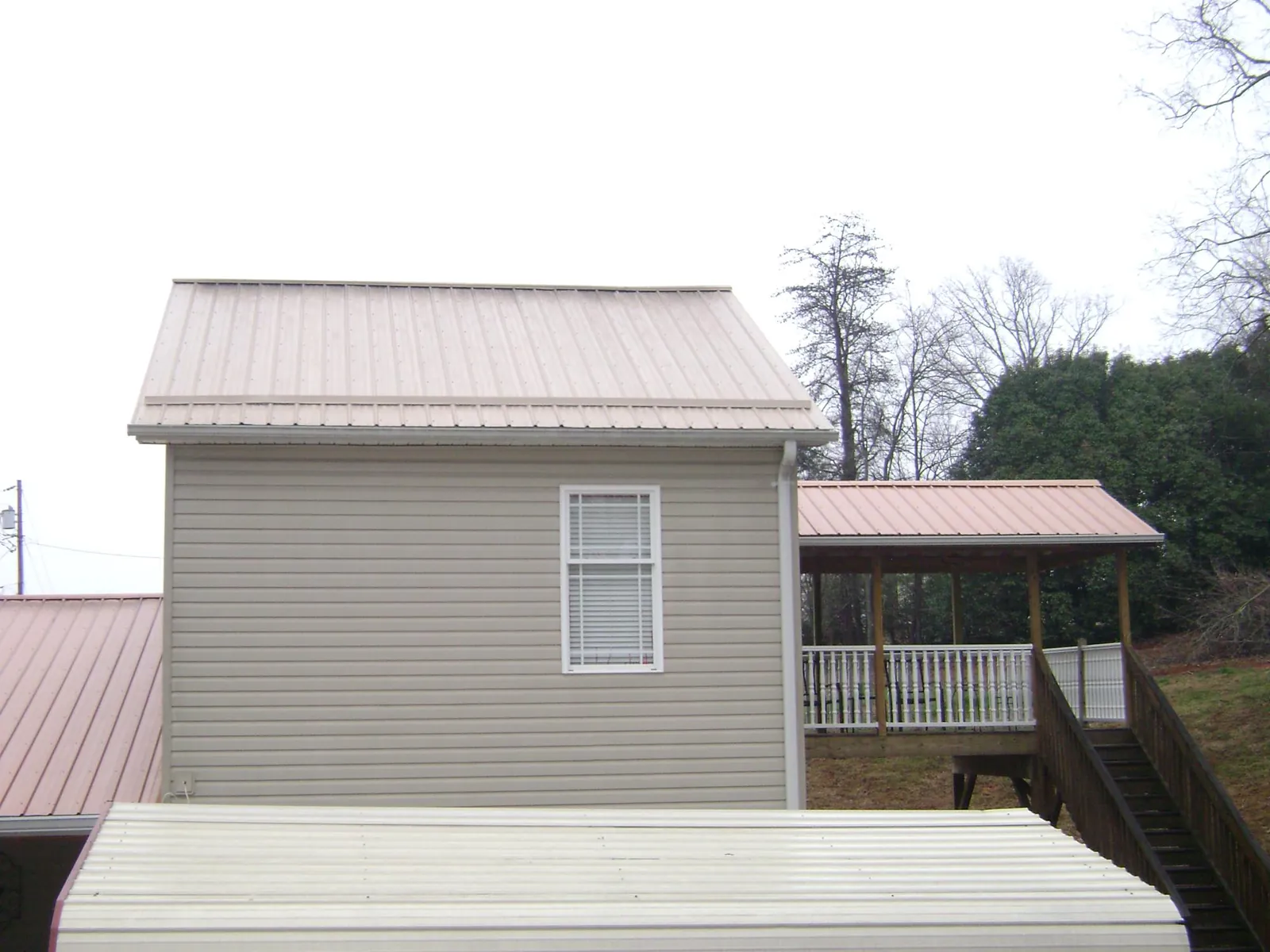Tan metal roofs on a two story addition and attached porch, from a Roof Replacement job in San Jacinto